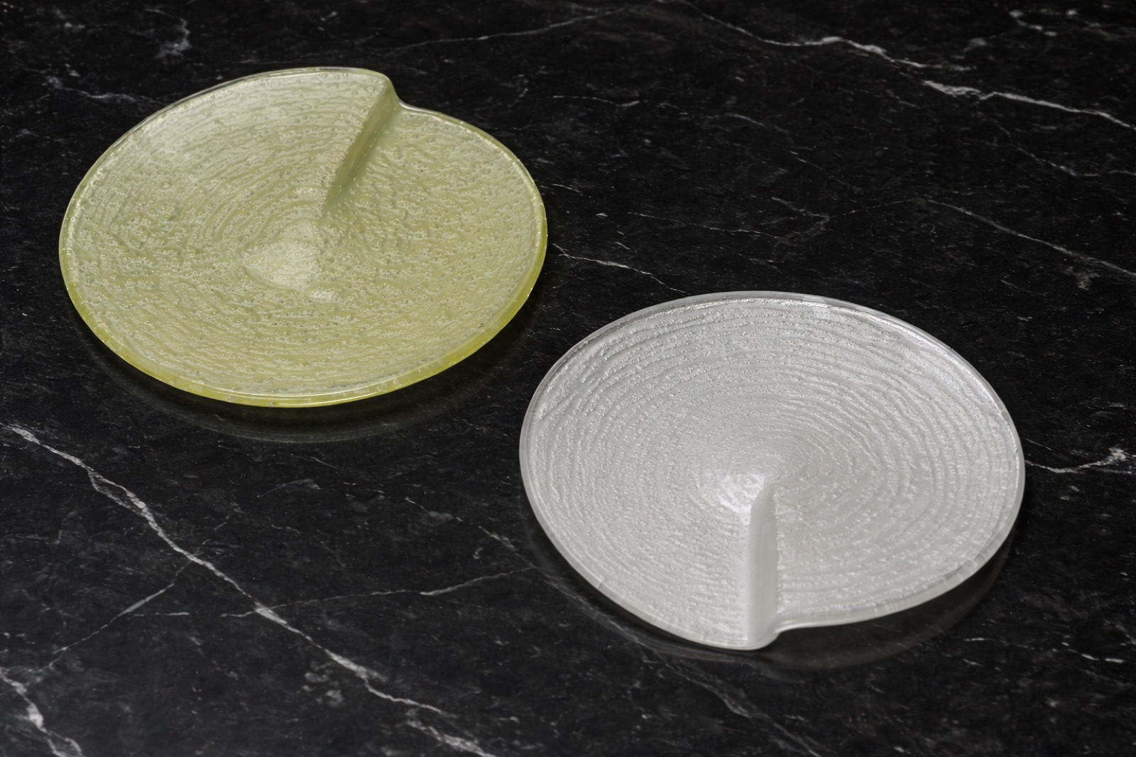 Two round notched glass plates in spring-yellow and pearl-white on black marble